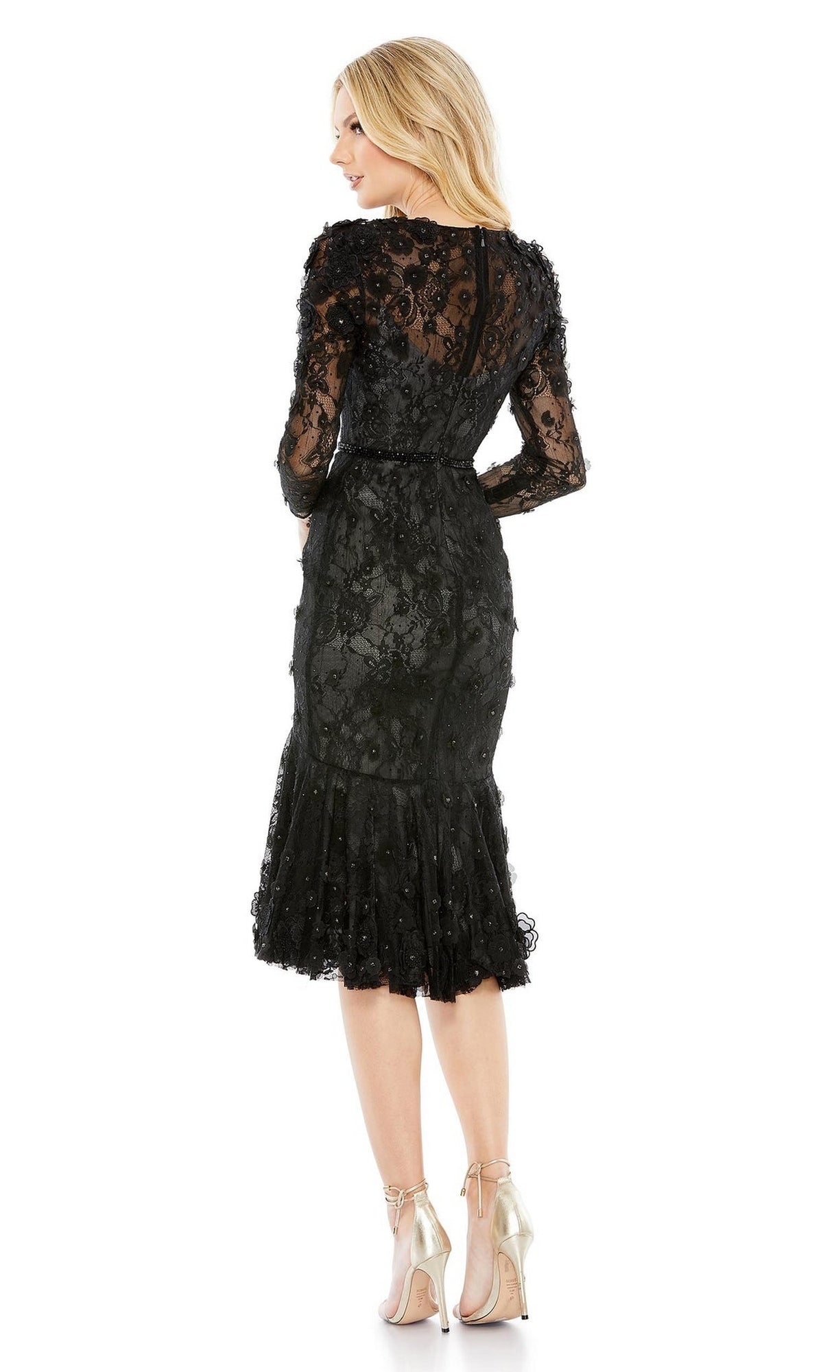 Woman wearing the Mac Duggal 67703 knee-length black party dress with sheer sleeves and floral embroidery, paired with high-heeled shoes, facing away from the camera.